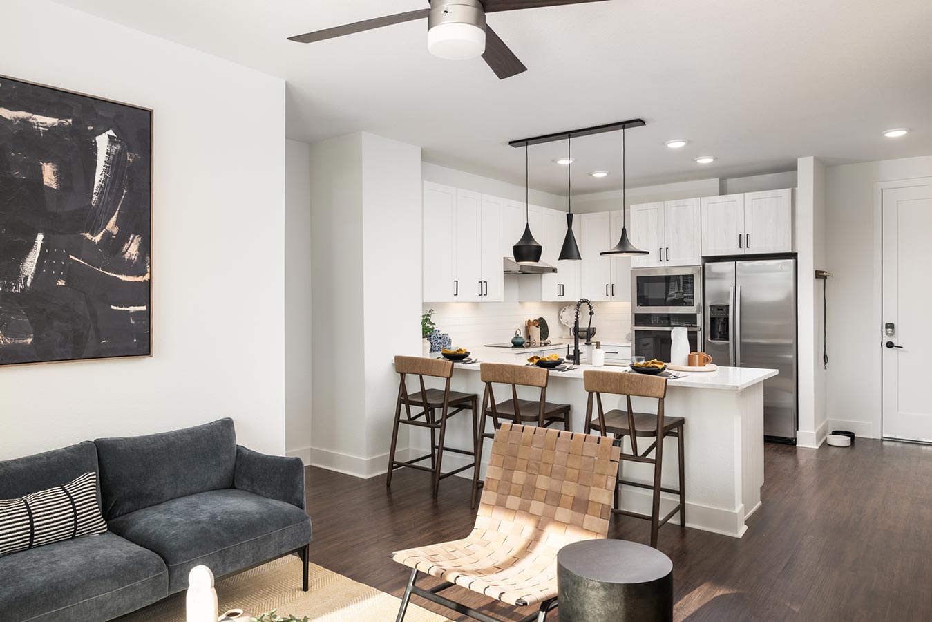 Open layout shows kitchen and living room with bar stools at the counter and couch
